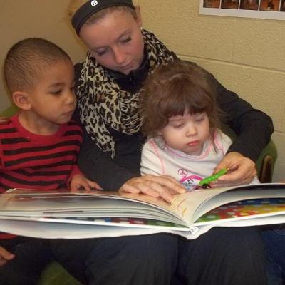 two young children reading a large picture book with an educator