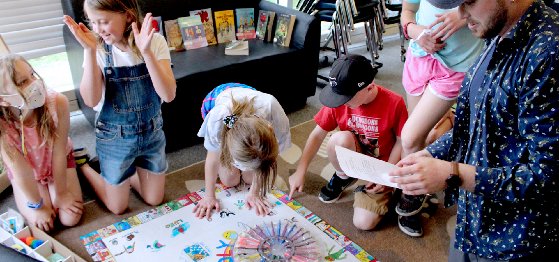 young male educator and group of school age children kneeling beside a homemade board game they created