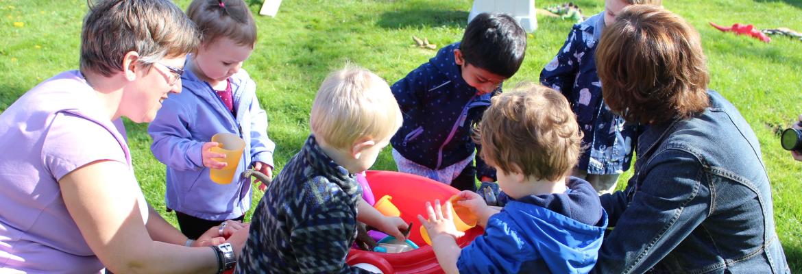 home child care provider and five children outside at a water table in spring