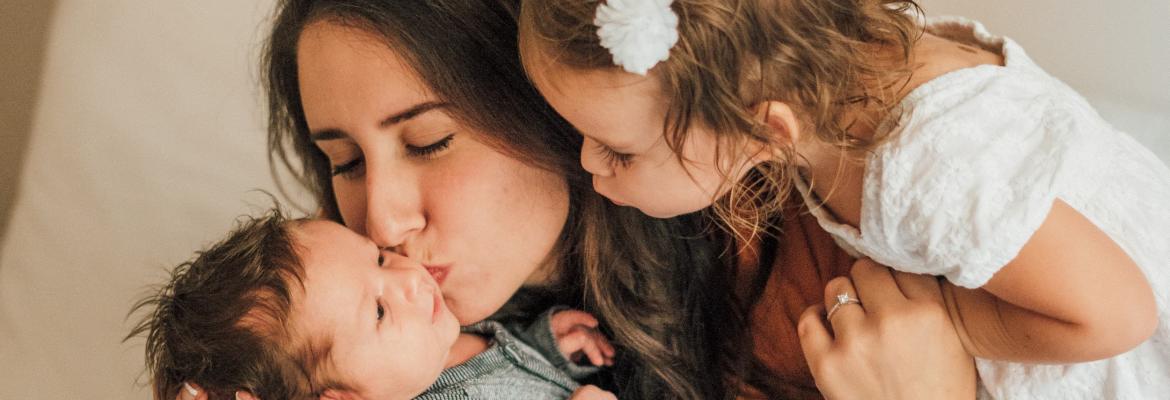 mom kissing baby with toddler over shoulder