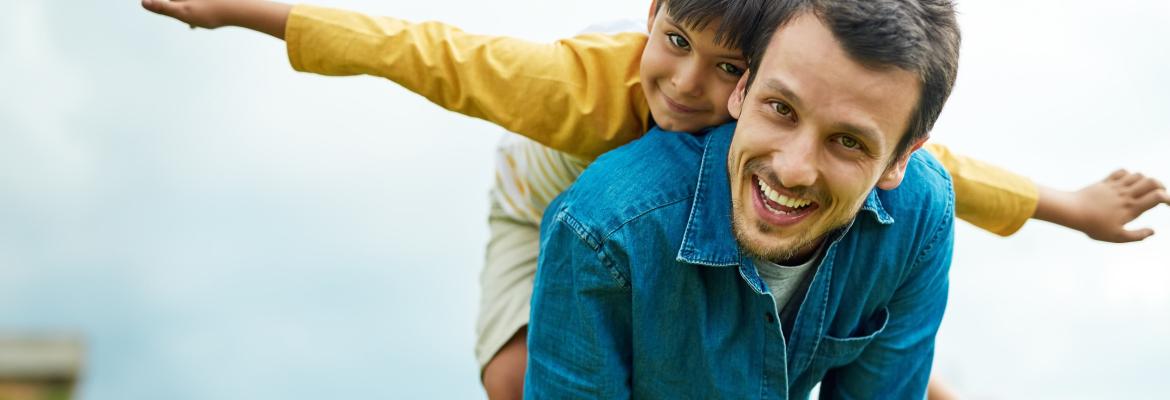 male educator with young child on his back with his arms spread like an airplane