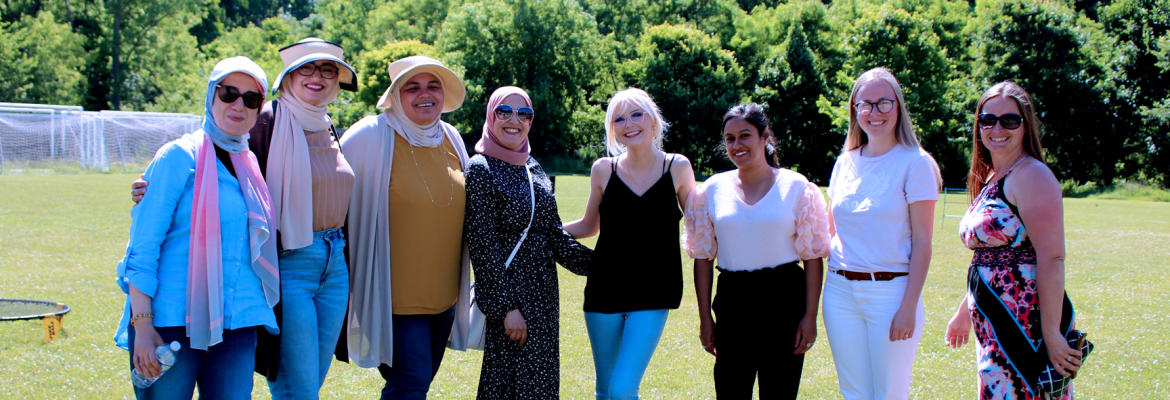 eight multi-cultural educators stand side by side on grass and smile at the camera